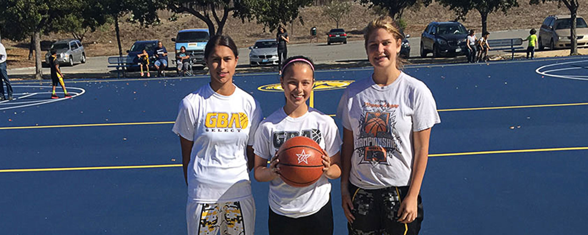 Three girls facing the camera holding a basketball